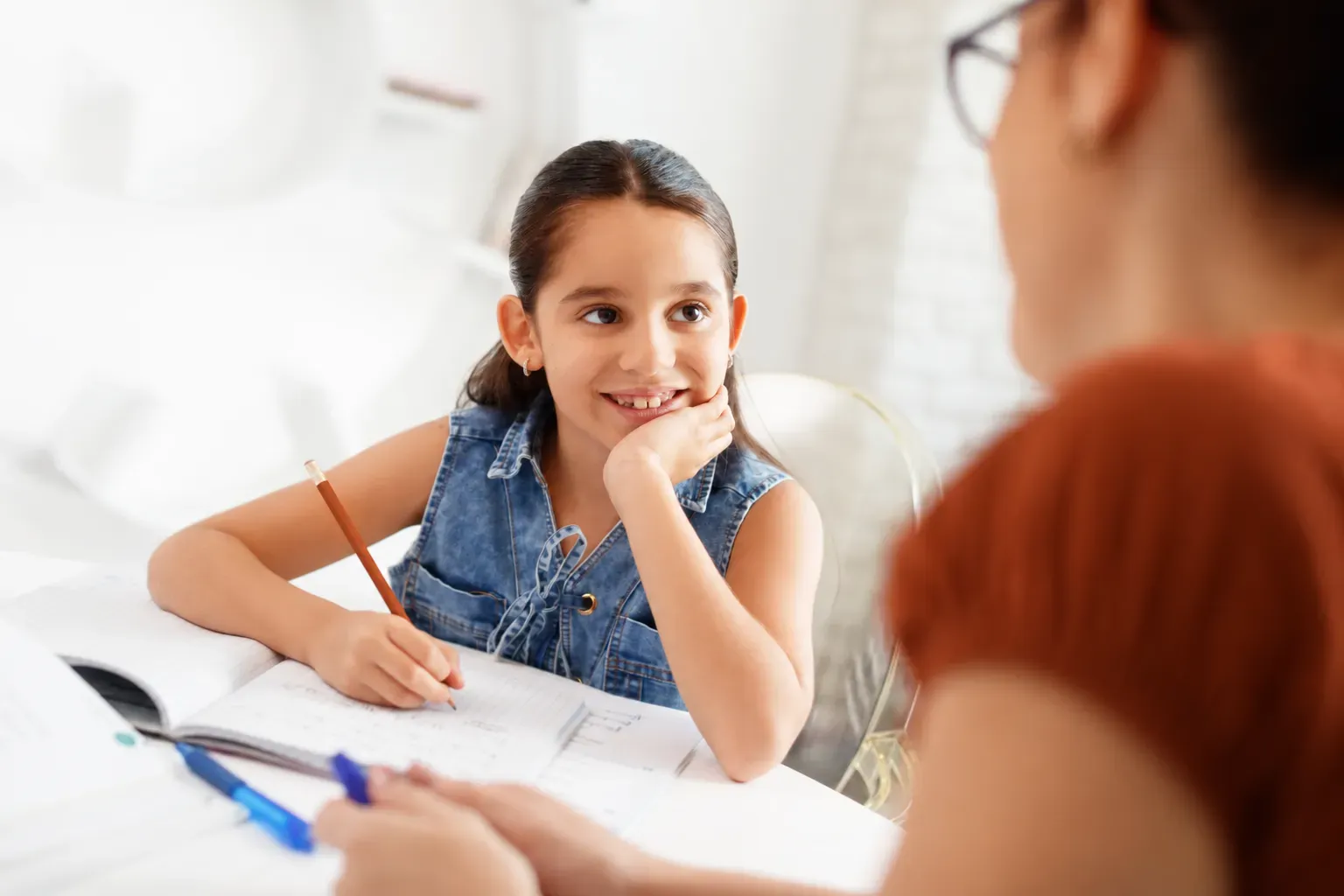 Ein Mädchen lächelt ihre Nachhilfelehrerin an und schreibt dabei in ihr Heft